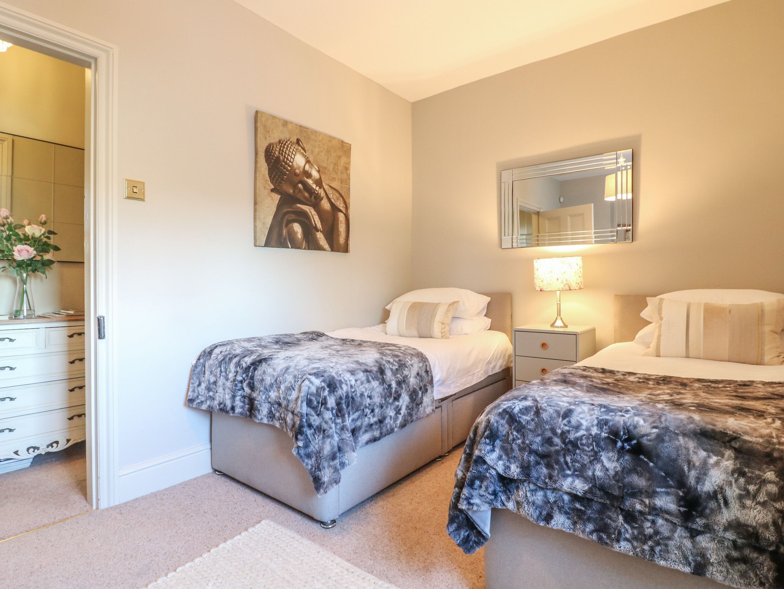 Een slaapkamer met twee bedden, een nachtkastje, een lamp, een spiegel en een schilderij aan de muur.