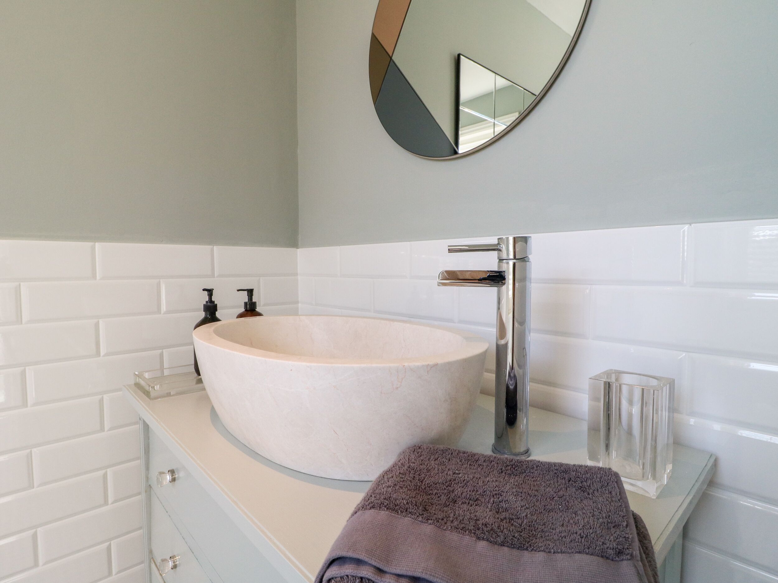 A bathroom with a round, beige sink, a modern faucet, and a mirror above the sink.