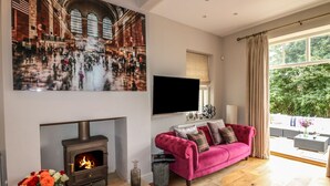 Uma sala de estar com lareira, um sofá rosa, um quadro grande de uma estação de trem e uma TV na parede.