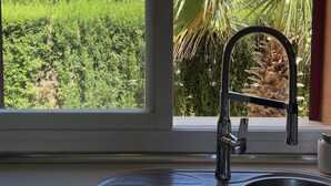 Une cuisine avec une fenêtre donnant sur une maison, un évier et un robinet.