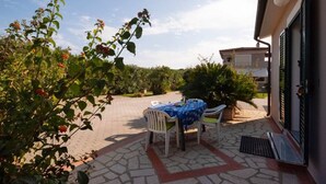 Une terrasse extérieure avec une table et des chaises, entourée de verdure et d’un bâtiment.