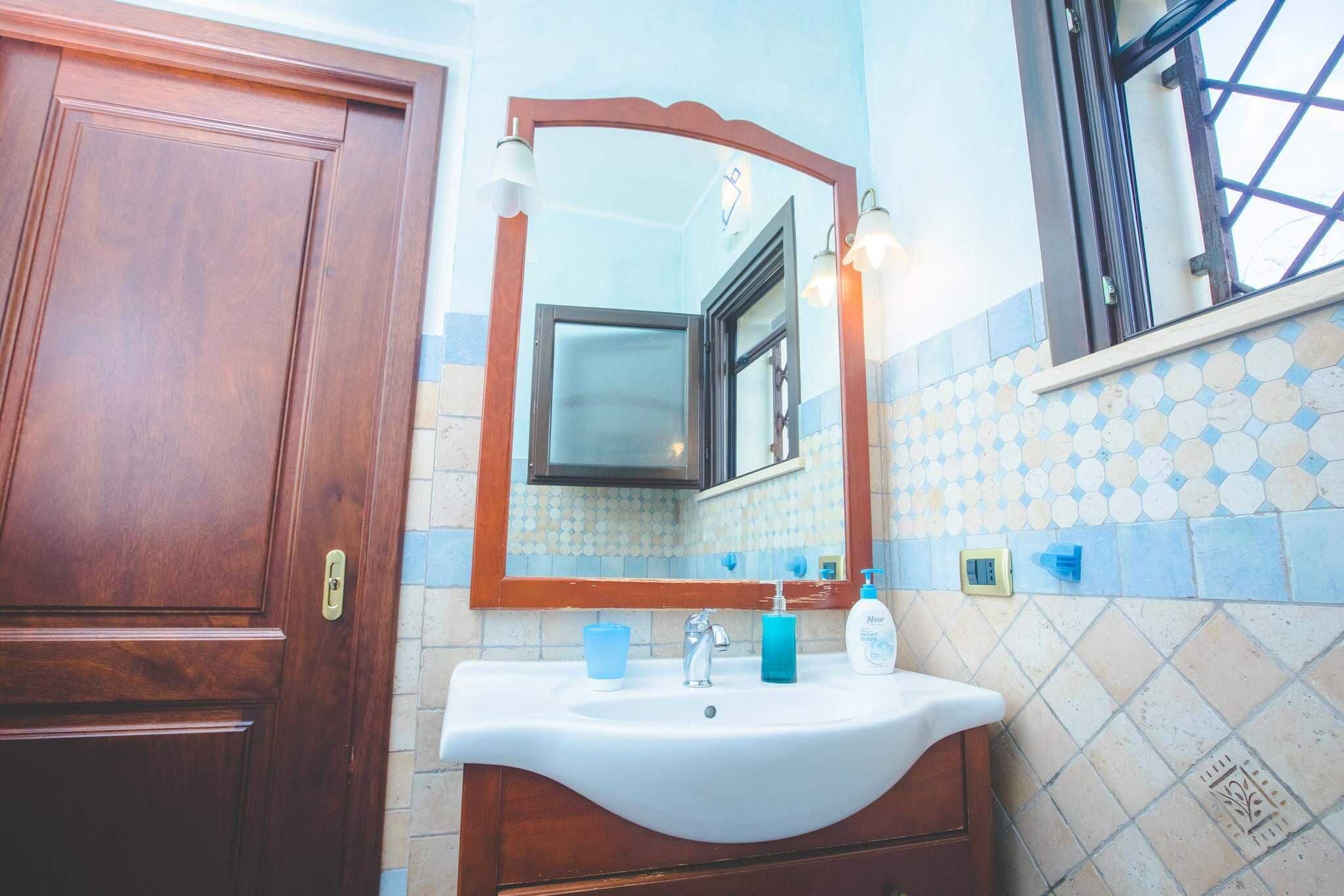 A bathroom with a wooden door, a white sink, a mirror, and a window with a black frame.