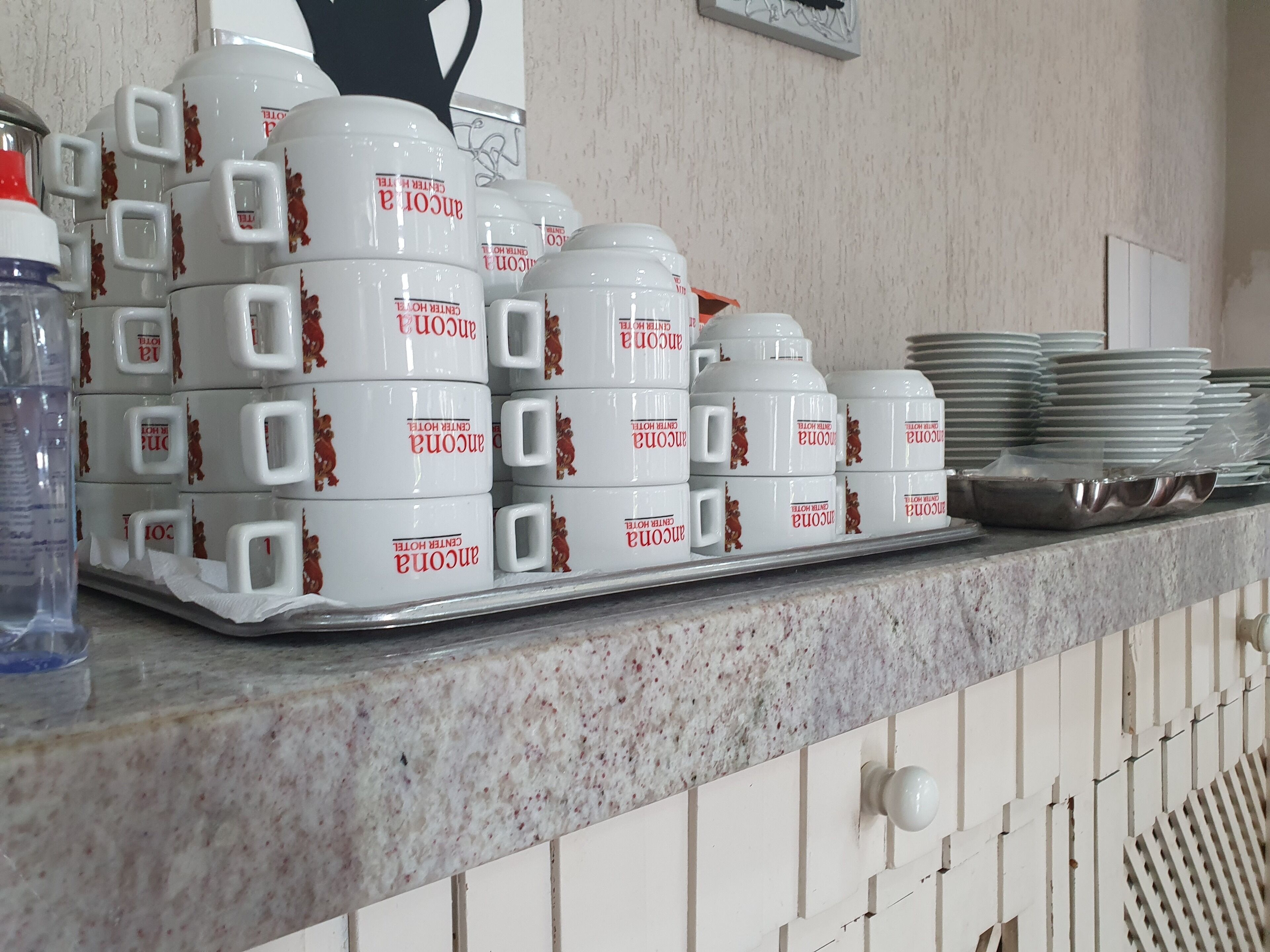 Stacks of white mugs with red text and handles on a kitchen counter.