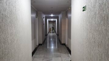 A long, narrow hallway with tiled floors and walls, featuring emergency exit signs and a door at the end.