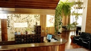 A reception area with a wooden reception desk, a computer monitor, and a potted plant. - Ancona Center Hotel (Amparo)