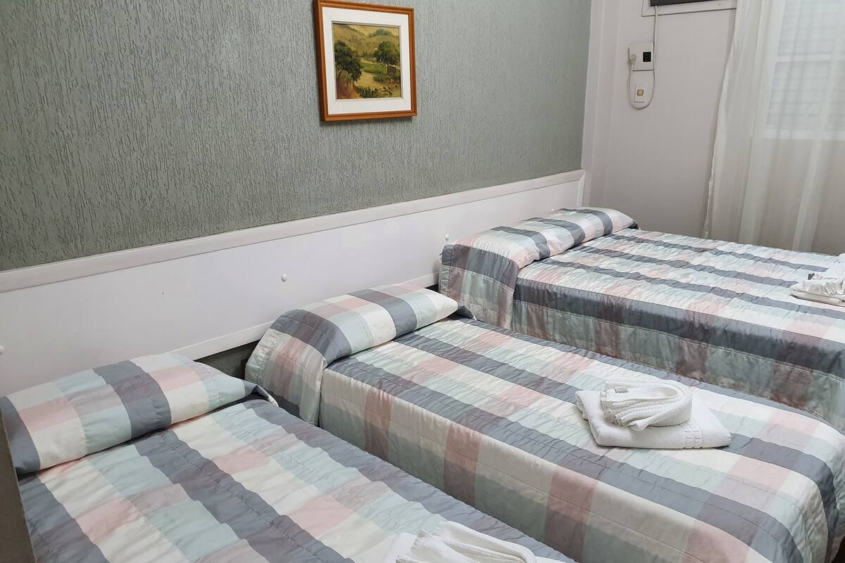 A hotel room with two beds, each with a checkered bedspread and pillows. There is a framed picture on the wall above the beds.