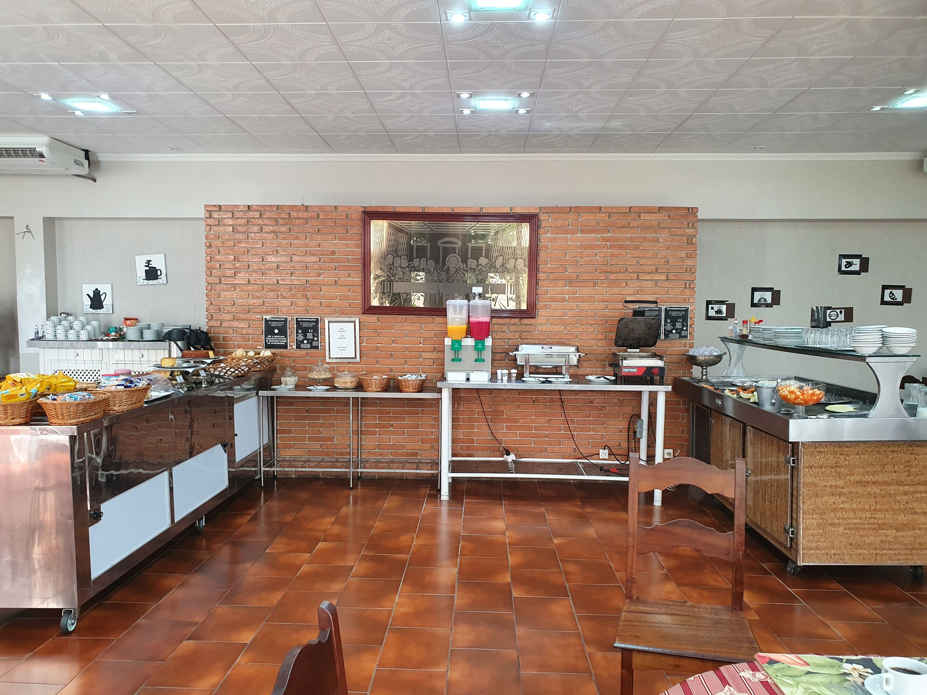A breakfast buffet area with a brick wall, tiled floor, and various food and drink stations.