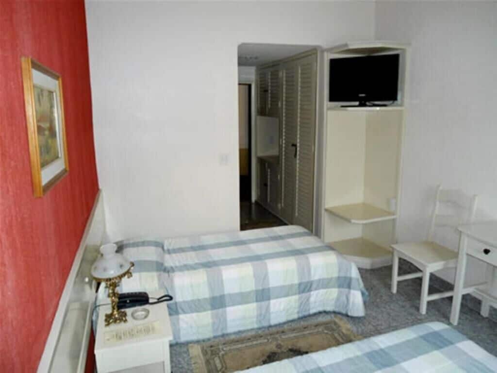A bedroom with a bed, a desk, a chair, a television, and a wardrobe.