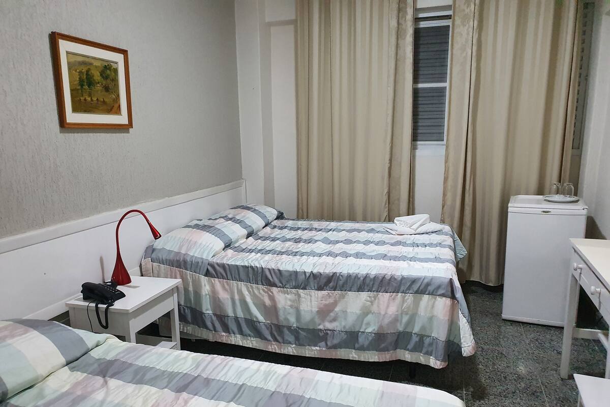 A hotel room with two beds, a desk, a chair, a small refrigerator, a telephone, and a painting on the wall.