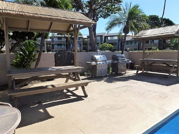 An outdoor patio with a pool, picnic tables, and barbecue grills.