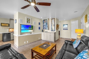 A living room with a television, a ceiling fan, a coffee table, a sofa, and a bookshelf.