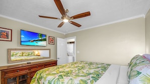 A bedroom with a bed, a ceiling fan, a television, and a door leading to a bathroom.