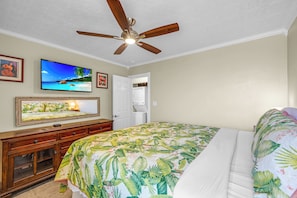 A bedroom with a bed, a ceiling fan, a television, and a door leading to a bathroom.