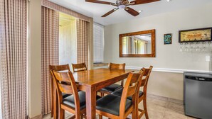 A dining area with a wooden table and chairs, a ceiling fan, a refrigerator, and a wall-mounted mirror.