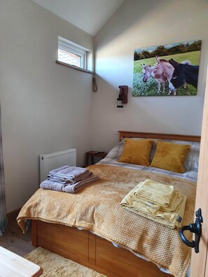 Un dormitorio con cama, radiador, ventana, un cuadro de animales y una mesita de noche.