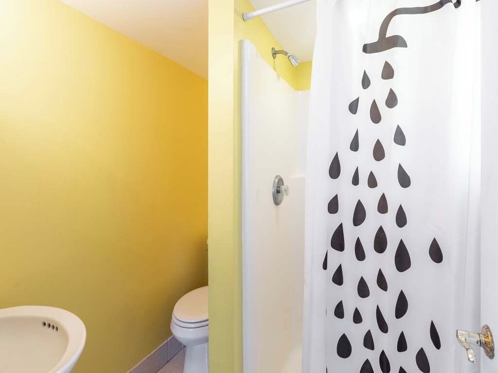 A bathroom with a yellow wall, a white sink, and a shower with a rain pattern curtain.