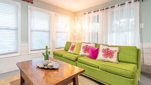 A living room with a green sofa, white curtains, and a cactus on the coffee table. - All Decked Out | Waterfront + Unique Dock House (Tybee Island)
