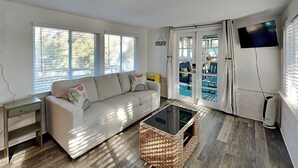 A living room with a sofa, a coffee table, a TV, and a sliding glass door leading to an outdoor area. - All Decked Out | Waterfront + Unique Dock House (Tybee Island)