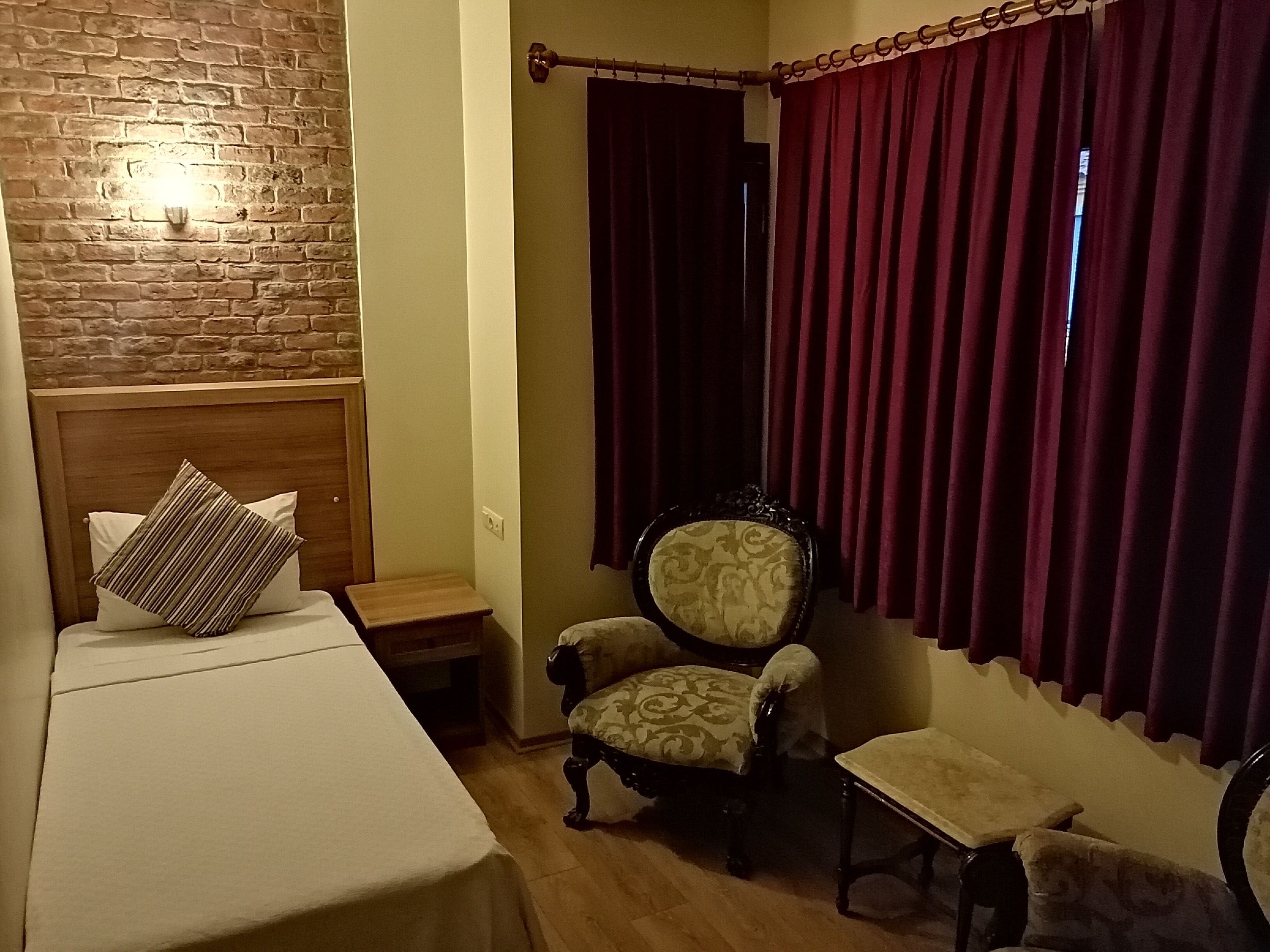 Um quarto com uma cama, uma cadeira, uma mesinha e uma cortina.