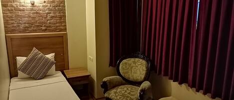 Um quarto com uma cama, uma cadeira, uma mesinha e uma cortina.
