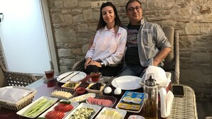 A couple seated at an outdoor table with a variety of food items and a bottle of oil. - Casa Callinos (Selçuk)