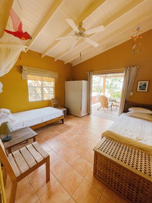 A room with two beds, a ceiling fan, a window with curtains, and a view of the outside.
