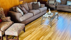 Een woonkamer met een houten trap, twee banken, gestreept fauteuils en een glazen salontafel.