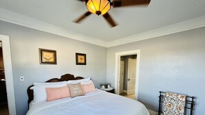 Een slaapkamer met een groot bed, een plafondventilator en twee ingelijste foto's aan de muur.