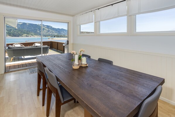 Un comedor con mesa de madera, sillas y vista a la playa a través de amplios ventanales.