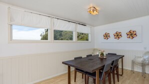 A dining area with a wooden table and chairs, white paneled walls, and three windows with white curtains. - Views for miles of the  Ocean and Bolinas Lagoon (Bolinas)