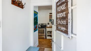 A hallway leading to a kitchen with a 'Please Remove Shoes' sign, a 'Welcome' sign, and a 'Hawaii' poster.