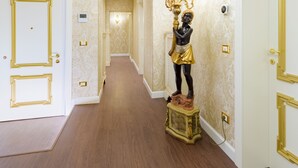 A hallway with ornate wallpaper, a statue, and a chandelier.