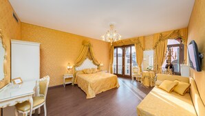 A hotel room with a large bed, a sitting area with a sofa, a glass table with a chair, and a television on the wall.