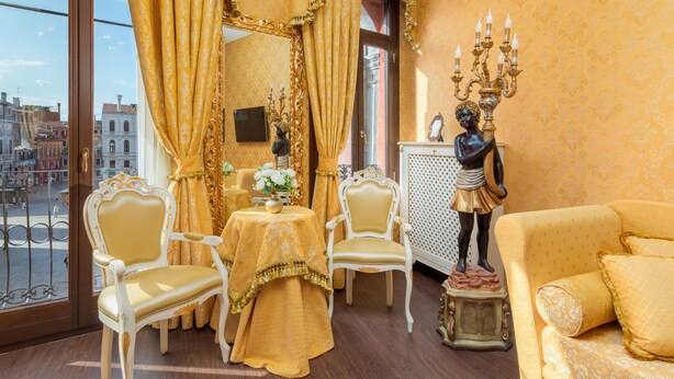 A room with a balcony view, ornate curtains, a statue, and a sofa.