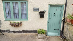 A quaint cottage with a green door and window, a mailbox, and a flower box. - Cholmley Cottage (Whitby)