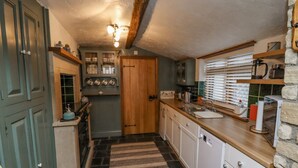 A compact kitchen with a stone floor, wooden cabinets, and a built-in oven. - Cholmley Cottage (Whitby)