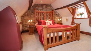 A bedroom with a wooden bed, stone wall, and a sloped ceiling. - Cholmley Cottage (Whitby)