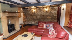 A cozy living room with a stone wall, a red leather sofa, a wooden coffee table, and a fireplace. - Cholmley Cottage (Whitby)