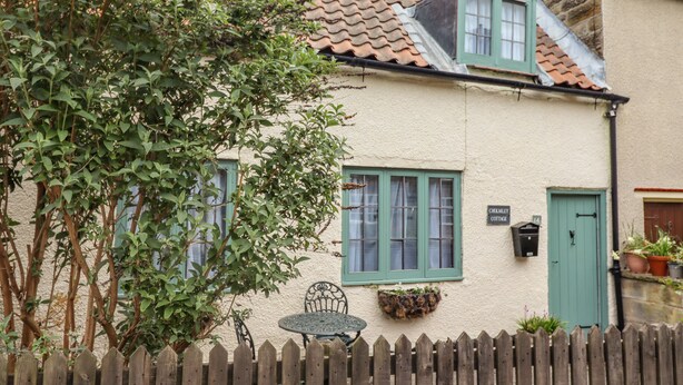 A quaint cottage with a picket fence, a small table, and a window with a green shutter. - Cholmley Cottage (Whitby)