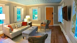 A living room with a sofa, ottoman, chair, and a flat-screen TV mounted on the wall.