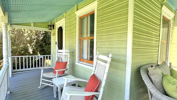 A porch with a rocking chair and a table, a wicker sofa, and a window with a number 4011 on the wall.