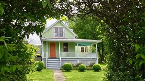 A green house with a porch, a front door, and a pathway leading to it.