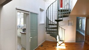 A modern interior with a spiral staircase, wooden flooring, and a sliding glass door leading to a kitchen area.