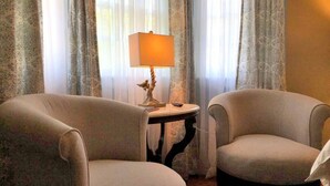 Una habitación con dos sillones, una mesita con lámpara y cortinas traslúcidas.
