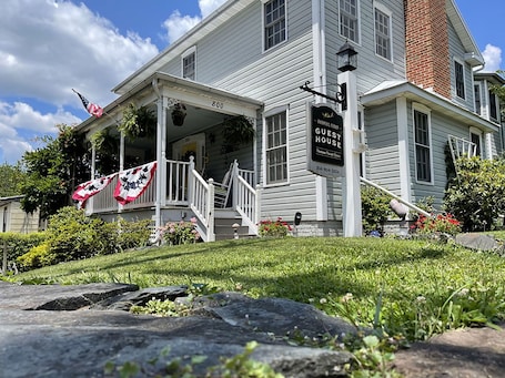 A two-story white building with a porch, a sign reading "Harper's Guest House," and a flag.