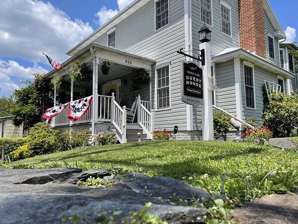 A two-story white building with a porch, a sign reading "Harper's Guest House," and a flag.