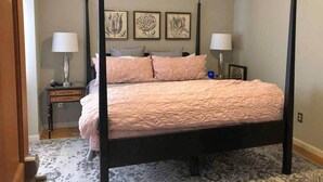 A four-poster bed with a pink quilt, two bedside tables with lamps, and three framed floral artworks on the wall. - The Cardinal Suite at Harpers Ferry Guest House (Harpers Ferry)