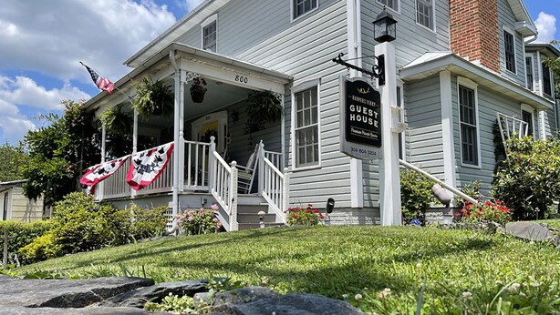 A two-story white building with a porch, a sign reading "Harper's Guest House," and a flag. - The Cardinal Suite at Harpers Ferry Guest House (Harpers Ferry)