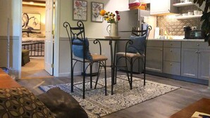 Un salón acogedor con un tapete estampado, una mesa de centro y un sofá. Se observa un comedor con una mesita y sillas. Se puede ver la cocina, con armarios y una encimera.