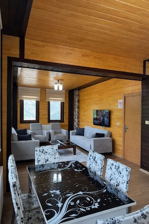 A modern interior with a wooden ceiling, a dining table with floral chairs, and a sofa set. - Şimo Suite Otel (Çaykara)